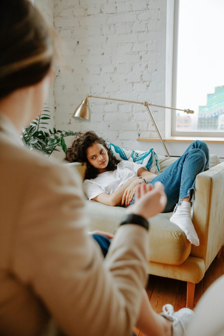 A therapist converses with a young adult on a sofa, focusing on mental health.