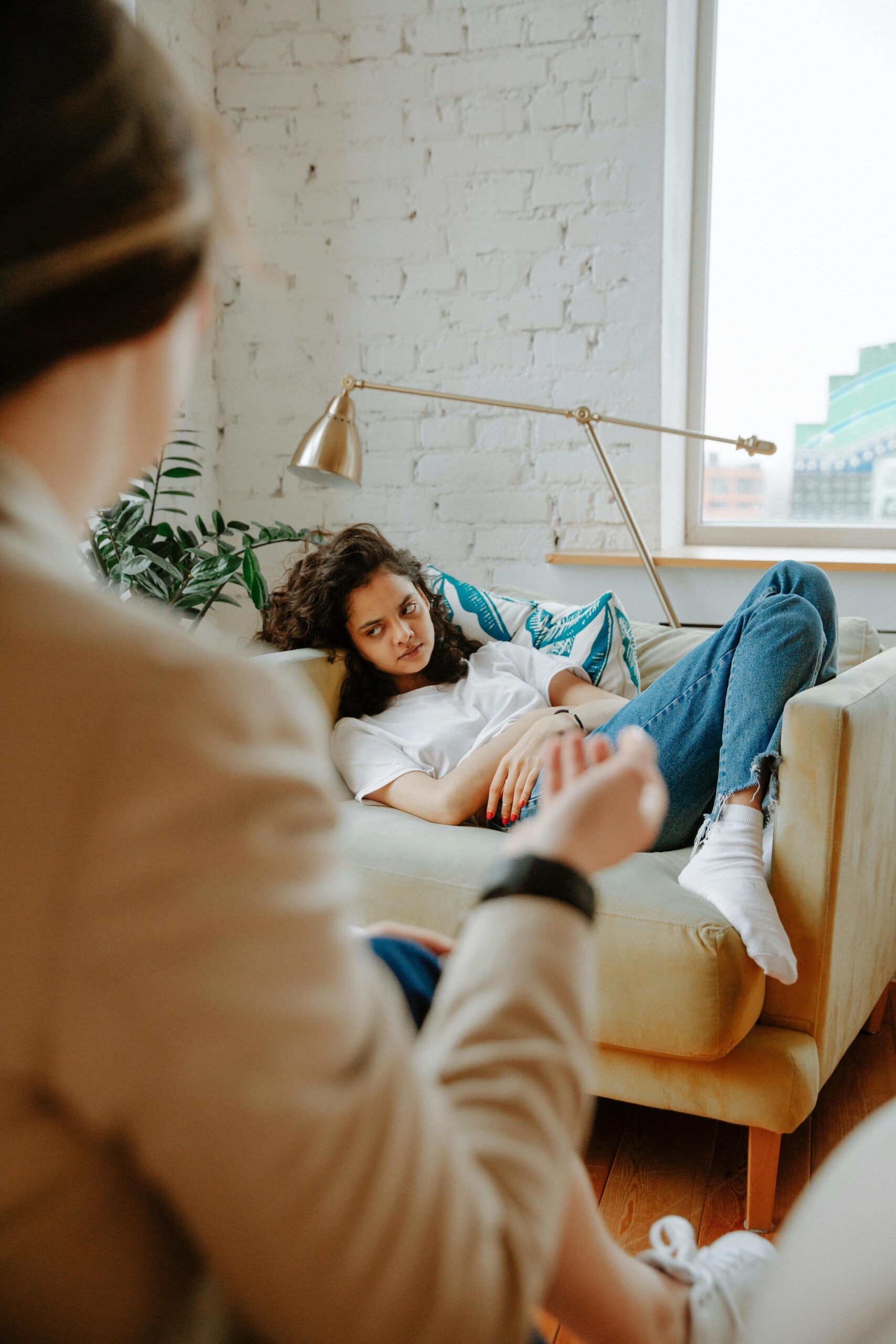 A therapist converses with a young adult on a sofa, focusing on mental health.